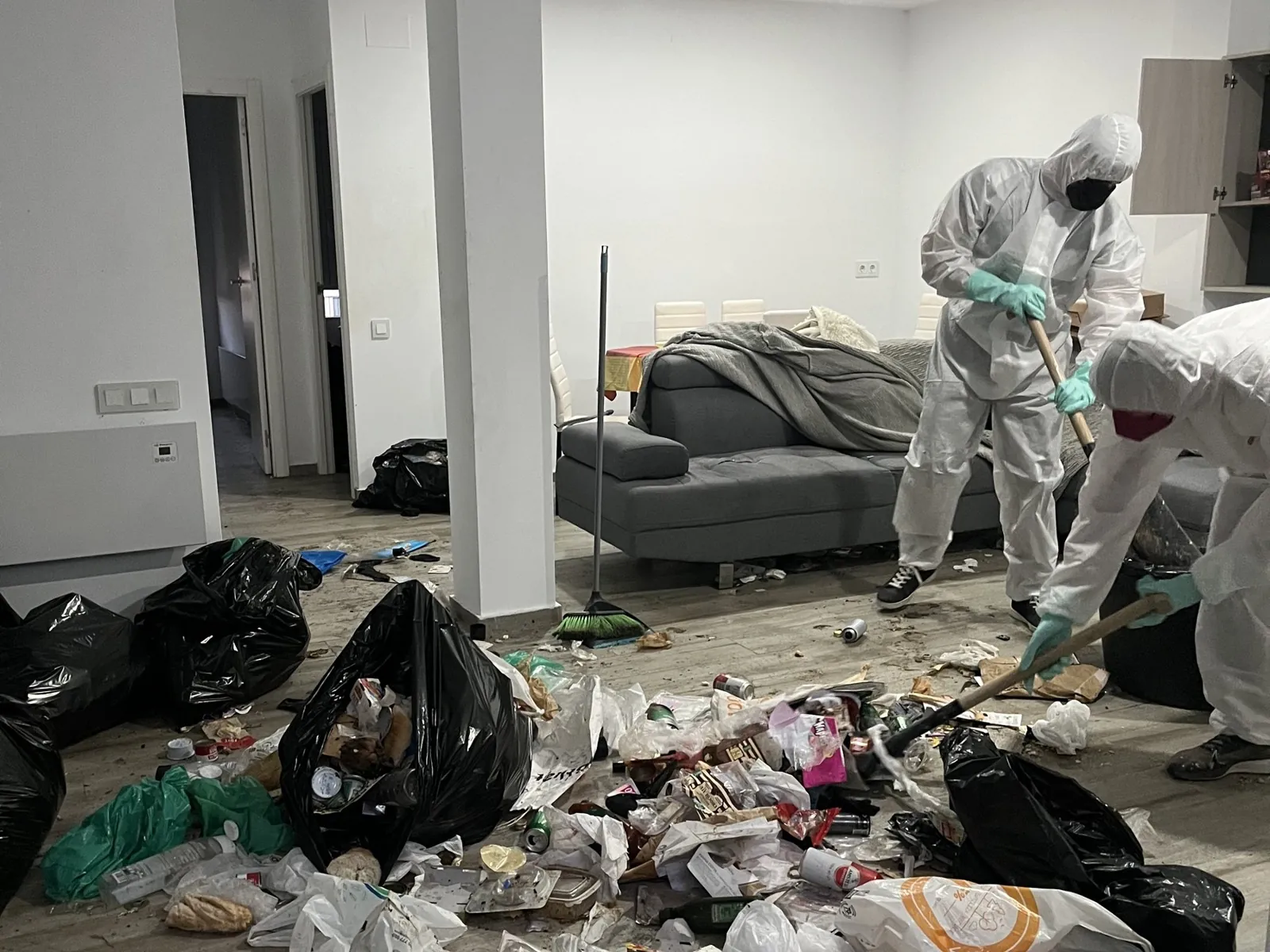 El salón antes de la limpieza, lleno de bolsas de basura y restos, con el equipo trabajando en trajes de protección